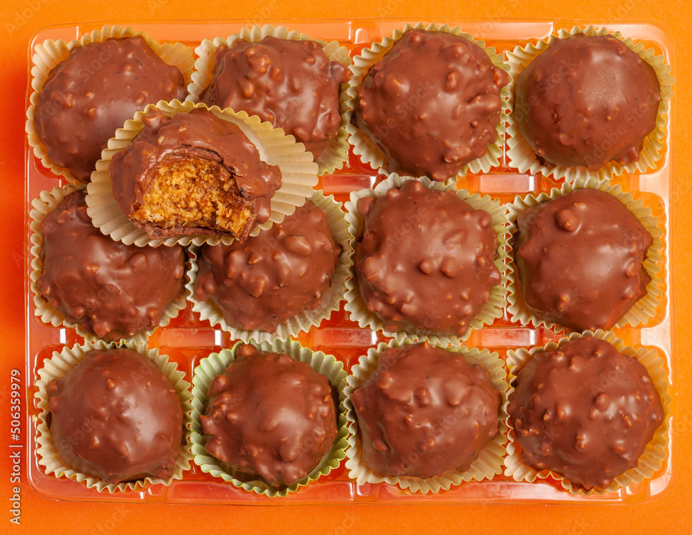Tasty chocolate candy ball shapes with filling and nuts, on orange background. Fill the entire frame, rectangle tray Tasty chocolate candy ball shapes with filling and nuts, on orange background. Fill the entire frame, rectangle tray