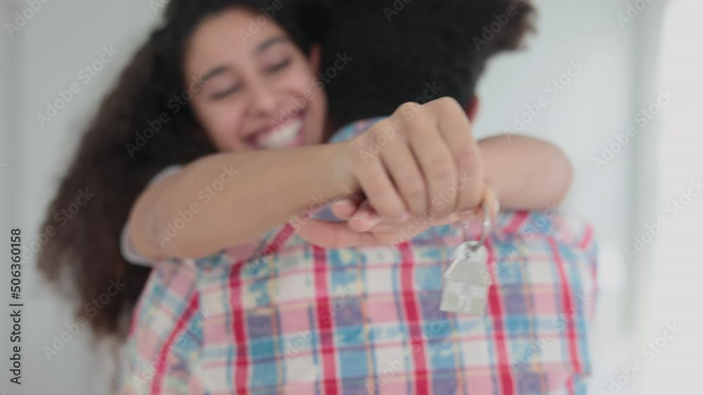 Young couple of homeowners is showing house keys and hugging in bright room spbi. 4k Close view of beautiful curly woman hugs man and holds keys in hand, looks with smile and poses for camera in Young couple of homeowners is showing house keys and hugging in bright room spbi. 4k Close view of beautiful curly woman hugs man and holds keys in hand, looks with smile and poses for camera in