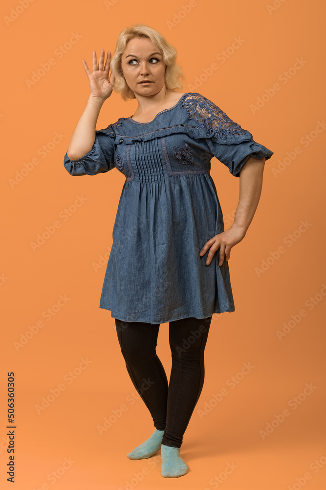 pretty blonde bbw woman in a blue dress put her hand to her ear and listens to gossip on a colored background pretty blonde bbw woman in a blue dress put her hand to her ear and listens to gossip on a colored background