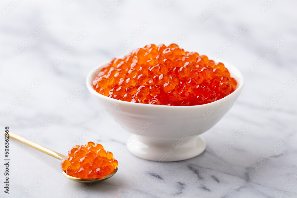 Red salmon caviar in white bowl on marble background. Close up. Red salmon caviar in white bowl on marble background. Close up.