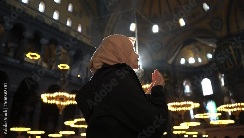 Asian muslim woman in scarf praying with her hands raised in Hagia Sopia Mosque photo