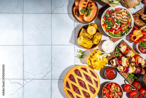 Various picnic barbeque food and drink flatlay. Summer bbq picnic food, assorted grilled meats, kebabs, vegetable, fruit salad, traditional picnic summer pie cake, sandwiches, top view copy space