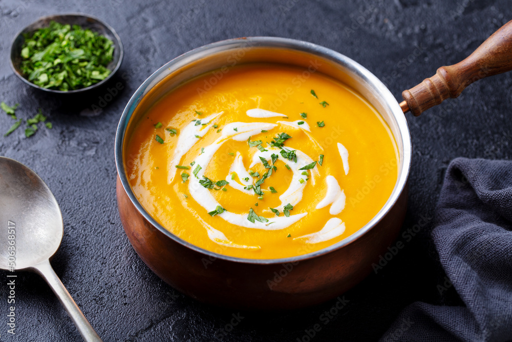 Pumpkin soup in copper saucepan. Black background. Close up. Pumpkin soup in copper saucepan. Black background. Close up.
