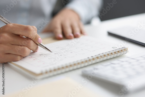 Closeup of person marking with pen and looking at date on calendar