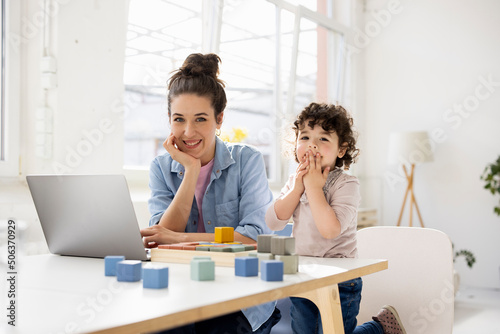 Mother working from home using laptop while daughter is playing with buiilding blocks photo