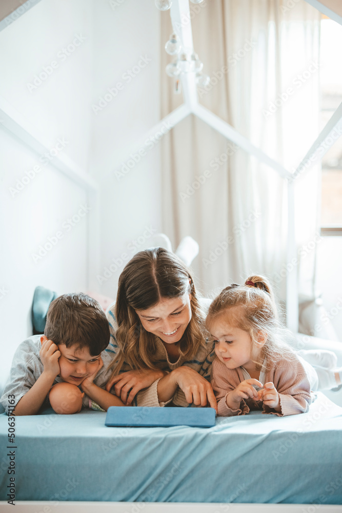 Smiling woman with son and daughter looking at tablet PC lying on bed Smiling woman with son and daughter looking at tablet PC lying on bed