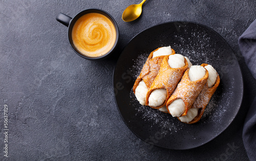 Cannoli Italian dessert on a black plate with cup of coffee. Grey background. Copy space. Top view. photo