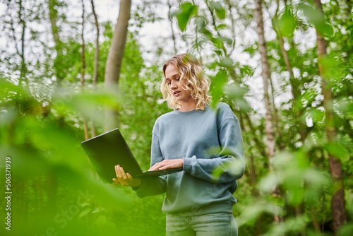 Freelancer using laptop amidst trees in forest photo