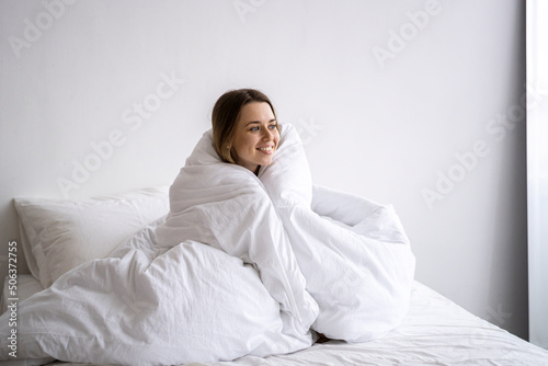 Happy woman wrapped in blanket sitting on bed at home photo