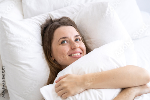 Happy woman embracing pillow lying on bed day dreaming at home photo