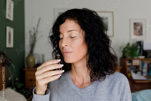 Woman smelling essential oil from bottle at home photo