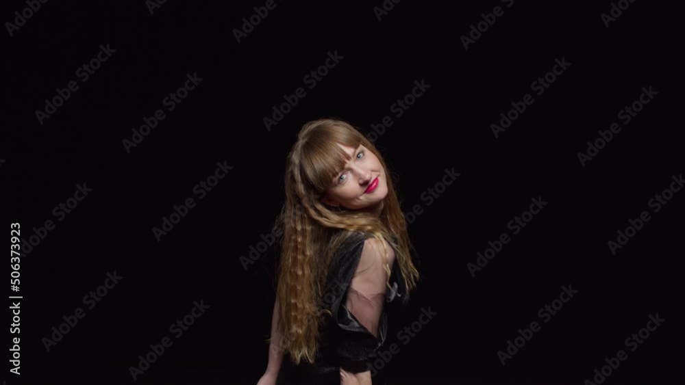 A young seductive woman in a dark dress dances sexily and smiles against a black background, fashion and glamour A young seductive woman in a dark dress dances sexily and smiles against a black background, fashion and glamour