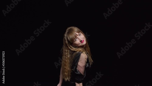 A young seductive woman in a dark dress dances sexily and smiles against a black background, fashion and glamour photo