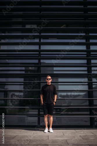 Portrait of men, in black shorts and black t-shirt, sunglasses on the street. Summer male portrait