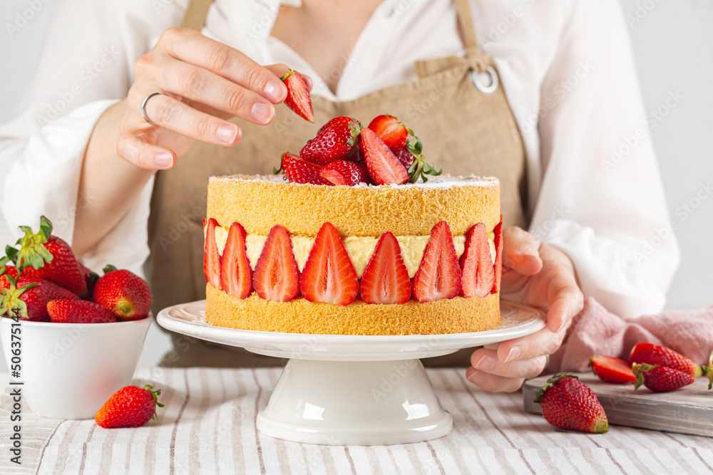 Woman cooking French Fraisier Cake made with two layer of Genoise Sponge, Diplomat Cream and Fresh Strawberries. Delicious Summer Cake with fresh berries.