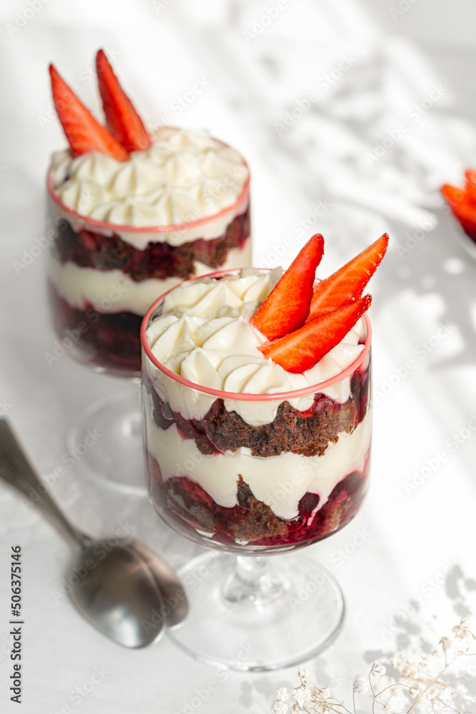 Chocolate brownie trifle with cream cheese and strawberries. Dessert in a wine glass. White table surface. Chocolate brownie trifle with cream cheese and strawberries. Dessert in a wine glass. White table surface.