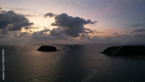 Beautiful sunset with clouds, sea and island. A small Thai ship is sailing. Clouds are reflected on the water. A lonely island stands in the distance. Top view from a drone. Calm ocean at sunset