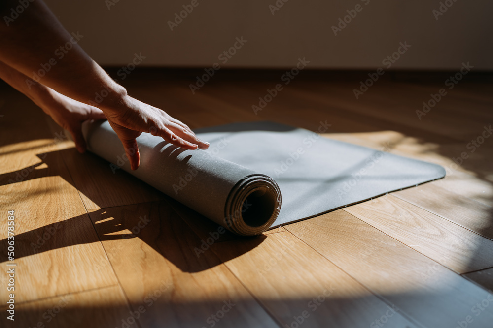 Close up of a woman hands is rolling up exercise mat and preparing to doing yoga. She is exercising on floor mat in morning sunshine at home