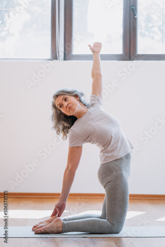 Full length view of the grey haired senior woman practicing yoga asana in studio or at home. Flexibility and sport concept