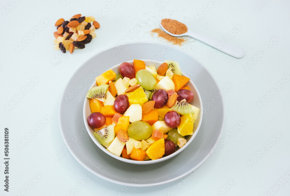 Close up on a bowl filled with a fresh and colorful fruit salad. Orange fruit, kiwi, papaya, melon, apple, almond. Brown sugar on the spoon Close up on a bowl filled with a fresh and colorful fruit salad. Orange fruit, kiwi, papaya, melon, apple, almond. Brown sugar on the spoon