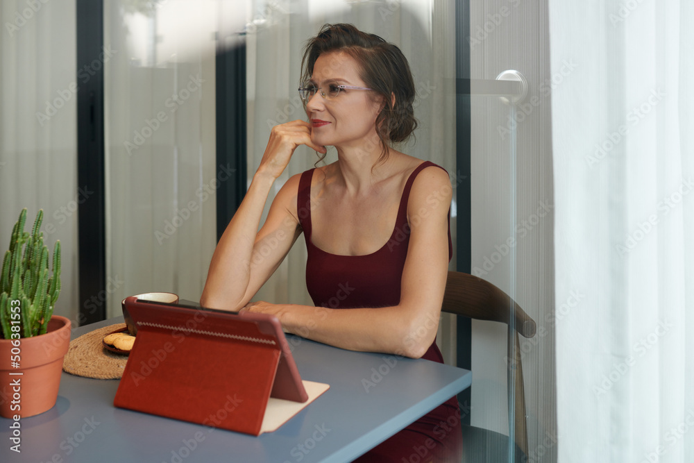 Portrait of positive elelegant businesswoman sitting at desk in her home office when working on tablet computer