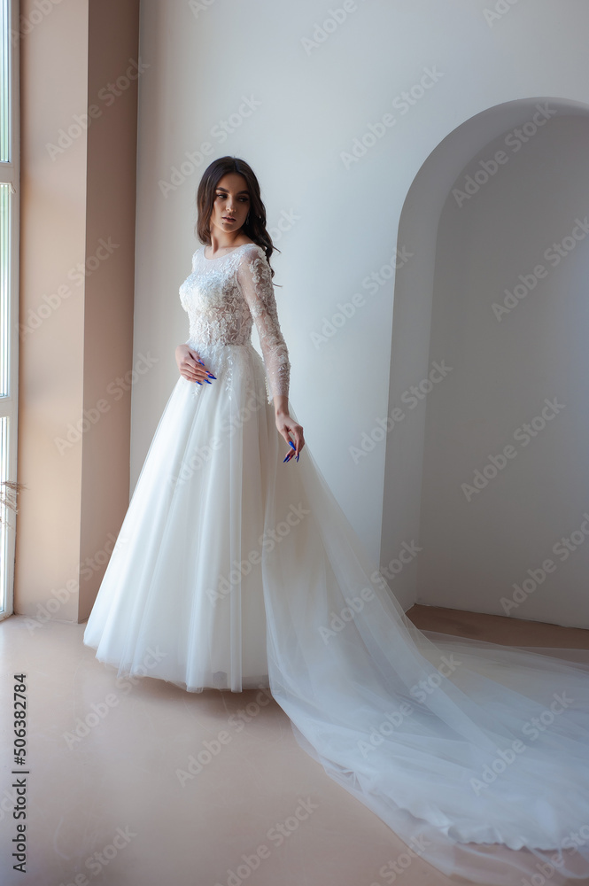 Full length portrait of young beautiful woman wearing white wedding dress. Elegant bride standing and posing