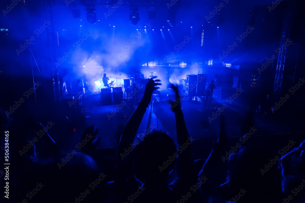 Silhouettes of concert crowd in front of blue stage lights. Fans during a life concert Silhouettes of concert crowd in front of blue stage lights. Fans during a life concert