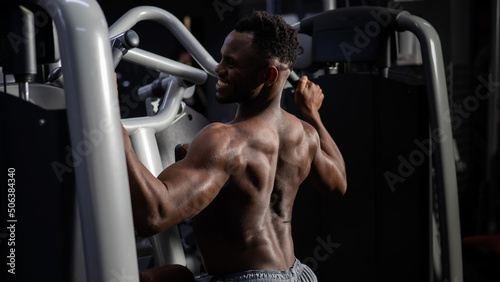 Fototapeta Naklejka Na Ścianę i Meble -  Shirtless african american man doing back exercises on a machine in the gym.
