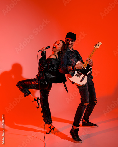 Fotografija Young Caucasian singer sings leaning on a guitarist on a background of red light