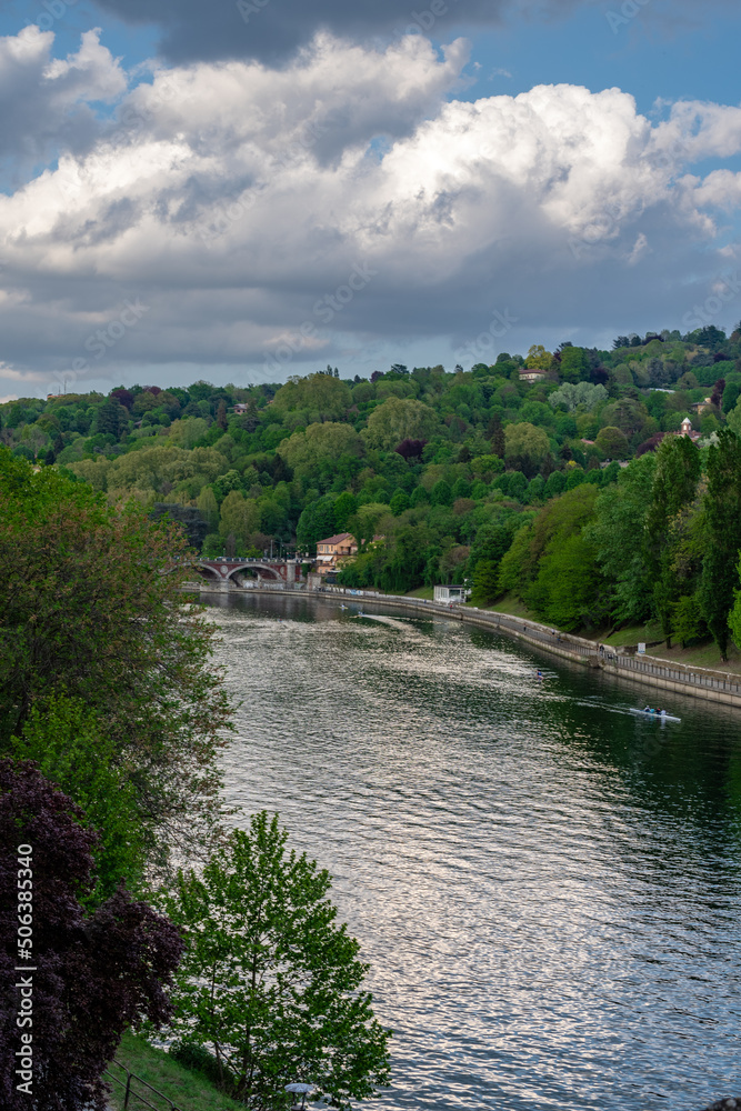 Natural landscape of the river Po in Torino on a spring afternoon. Green and leafy trees. Cloudy sky. And an old bridge that crosses the river.