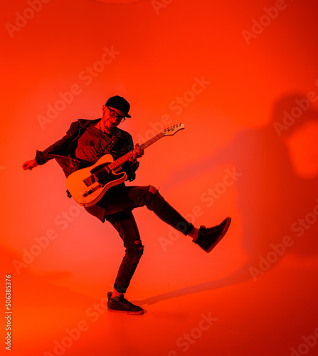 Fotografiet The young guitarist emotionally plays the electric guitar and jumps on a red lig