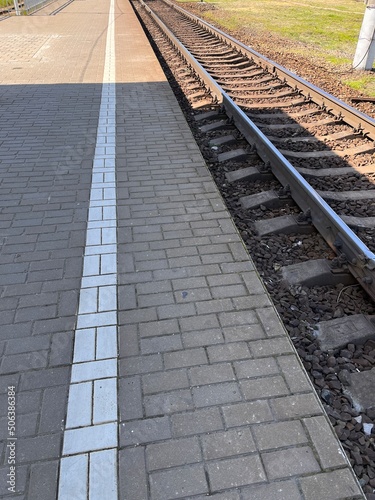 Fototapeta Naklejka Na Ścianę i Meble -  Paved platform on the railway station. White stripe on the perron in front of railroad