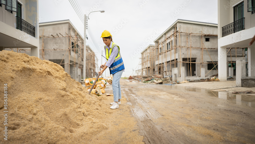 custom made wallpaper toronto digitalFemale construction worker with a vest and hardhat standing on dirty wet street, digging sand dirt with a shovel at residential house construction site. Full length of woman laborer is working strong.