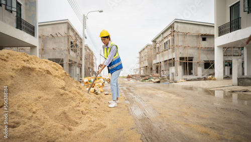 Wallpaper Mural Female construction worker with a vest and hardhat standing on dirty wet street, digging sand dirt with a shovel at residential house construction site. Full length of woman laborer is working strong. Torontodigital.ca