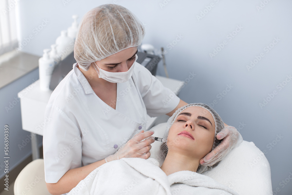 Woman gets injection in her face. Beauty woman giving botox injections. Young woman gets beauty facial injections in the cosmetology salon. Face aging injection. Aesthetic Medicine, Cosmetology Woman gets injection in her face. Beauty woman giving botox injections. Young woman gets beauty facial injections in the cosmetology salon. Face aging injection. Aesthetic Medicine, Cosmetology