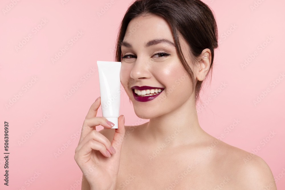 Smiling young woman holding cosmetics mockup tube, facial cream template jar. Pretty girl with healthy glowing skin, perfect makeup, bare shoulders advertise natural skincare or make-up beauty product Smiling young woman holding cosmetics mockup tube, facial cream template jar. Pretty girl with healthy glowing skin, perfect makeup, bare shoulders advertise natural skincare or make-up beauty product
