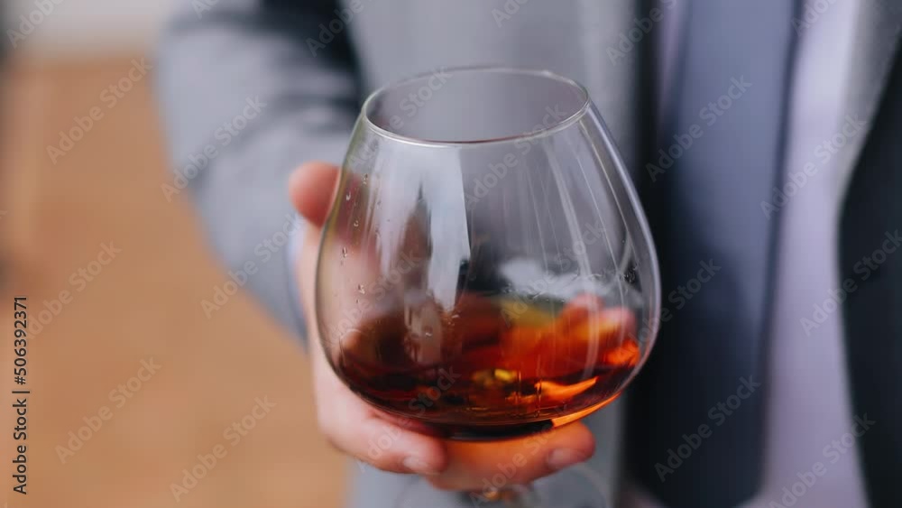 A man is holding a glass of cool-colored alcohol in his hands. Shooting in close-up A man is holding a glass of cool-colored alcohol in his hands. Shooting in close-up