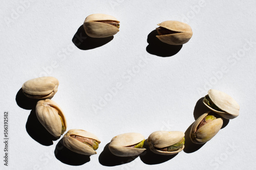 flat lay of cracked green and salty pistachios in shape of smile on white background