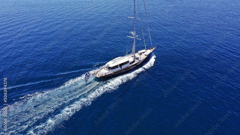 Aerial drone birds eye view photo of beautiful sailboat with blue sails cruising in the deep blue Aegean sea, Greece