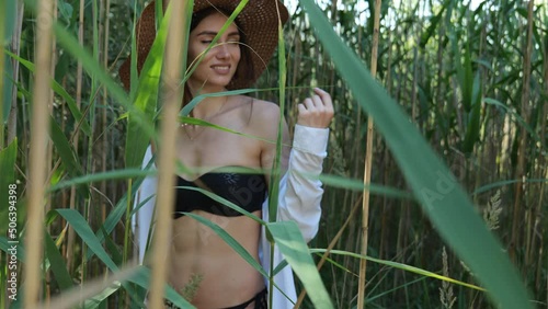 View through long green plants on a brunette woman in a hat and black swimsuit. Beautiful woman in the jungle