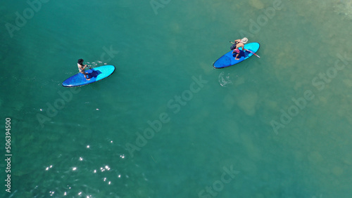 Aerial drone view of couple exercising sup board in turquoise tropical clear open sea