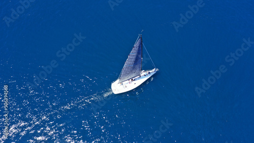Aerial drone birds eye view photo of beautiful sailboat with blue sails cruising in the deep blue Aegean sea, Greece