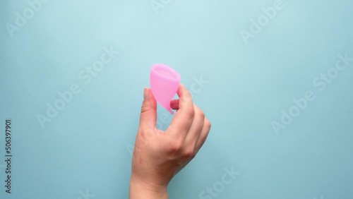 Ditching the tampon and  menstrual pad in favor of a menstrual cup. The woman's hand removes the tampon and sanitary napkin and puts the menstrual cup on the table. Footage on a blue plain background photo