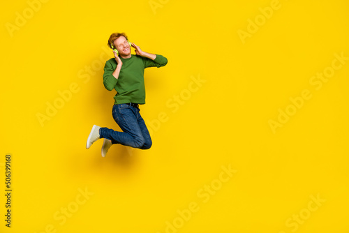 Full length photo of cool dreamy guy dressed sweater earphones enjoying music empty space isolated yellow color background