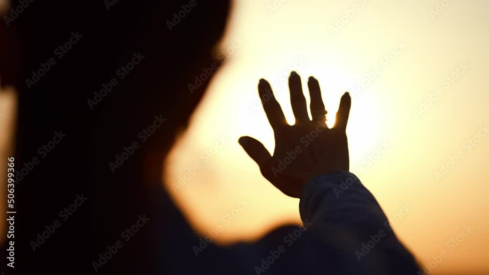 Silhouette of a woman with a hand catching the sun's rays at sunset. View from the back of a young woman at sunset. Silhouette of a woman with a hand catching the sun's rays at sunset. View from the back of a young woman at sunset.