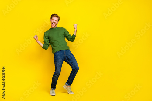 Full length photo of pretty lucky man wear green pullover rising fists empty space isolated yellow color background