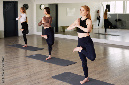 Group of women practicing yoga lesson, standing in lotus exercise, working out, indoor full length, studio background