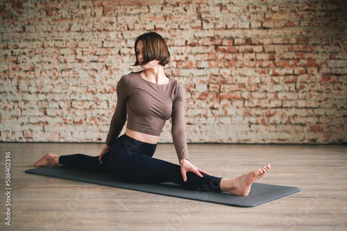 Young athletic woman is sitting on mat in longitudinal splits in yoga studio. The concept of stretching and healthy lifestyle
