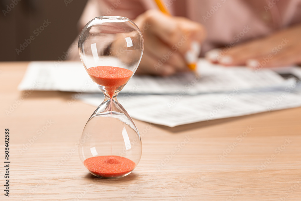 Hourglass with time running out and student hand testing in exercise and passing exam carbon paper computer sheet with pencil in school test room, education concept Hourglass with time running out and student hand testing in exercise and passing exam carbon paper computer sheet with pencil in school test room, education concept