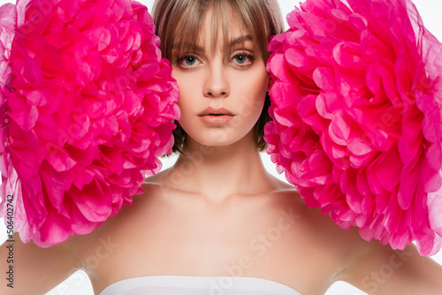blonde young woman looking at camera near bright pink flowers isolated on white